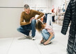 Father Helps Young Daughter Try On Shoes During Shopping Trip