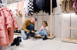 A caring father kneels in the middle of a clothing store to tie his daughter's shoelaces.
