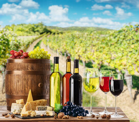 Wall Mural - Wine still-life. Bottles of wine, glasses of wine and grapes on wooden table and blurred vineyard at the background.