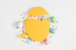 Easter decor concept. Frame made in shape of an Easter egg with colorful Easter eggs and sugar sprinkled candies on white background.Top view. Flat lay.