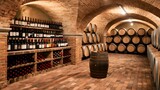 Fototapeta Lawenda - A rustic wine cellar with brick arches. On the left, there's a shelf displaying various bottles of wine. Adjacent to it, wooden barrels are neatly arranged on racks, some of which are stacked on top