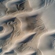 The warm sunset light accentuates the intricate patterns and shadows on the desert sand dunes from an aerial perspective.