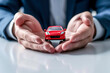 Concept of car insurance. Hands protecting red toy auto on the table