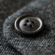 Macro photography of a single dark button on a finely textured piece of knitwear, highlighting the intricacies of woven garments.