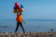 Cheerful boy standing with balloons on lake shore on summer day