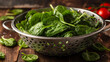 raw fresh spinach with drops in a colander on a rustic wooden table.