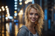Portrait of a smiling blonde girl with blue eyes in the evening city in rainy weather.