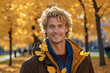 Portrait of a smiling blond man with blue eyes in an autumn park in sunny weather