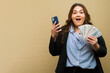 Excited plus-size woman holding a phone and fan of money in a studio with some copy space