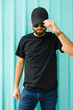 Stylish hispanic man in black t-shirt and cap casually holding his cap, set against a turquoise backdrop, ideal for a mockup