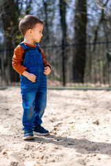 Sticker - A young boy in a blue overalls stands in the sand. He is looking at something in the distance