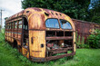 Abandoned rusty yellow school bus in overgrown outdoor setting 