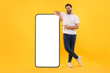 Canvas Print - Man pointing at huge mobile phone with empty screen on dark beige background. Mockup for design