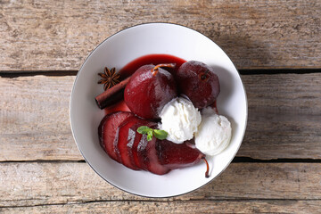 Tasty red wine poached pears and ice cream in bowl on wooden table, top view