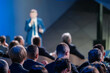 Focused view of a corporate leader speaking to an engaged audience at a professional business conference. The blurred foreground emphasizes the speaker.