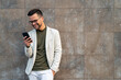 © Dorde - Business man and smartphone for reading notification, mobile chat and social network. Happy male scroll on cellphone, news app and search digital information against a wall.