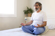Mature adult man relaxing, doing meditation sitting on bed at home. Male meditating in the morning. Copy space.