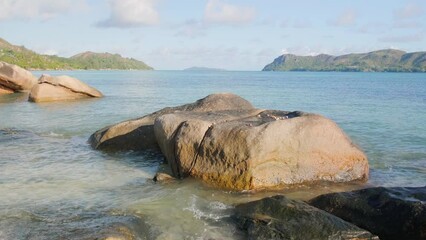 Poster - A large rock sits in the ocean near a beach. The water is calm and the sky is clear