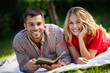 © peopleimages.com - Portrait, happy couple and nature for reading book in park with green grass, together and picnic blanket. Woman, man and fiction story for hobby in outdoor with happiness, relaxing and romance