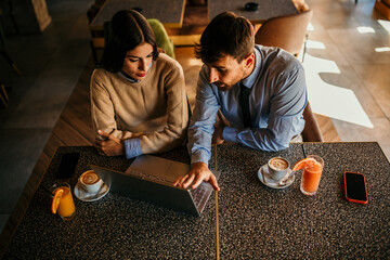 Wall Mural - A Latin businesswoman and her caucasian male colleague casually work together in a cafe bar on a laptop.