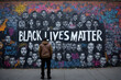 An African American man looking at graffiti artwork on wall in moving tribute to victims of racial, social injustice with the words 'Black Lives Matter' demanding justice and equality for minorities.