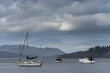 Beautiful landscape image of leisure boats on Lake Windermere in Lake District during overcast Spring afternoon with mountain backdrop