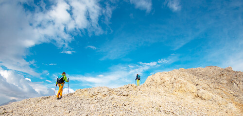 Wall Mural - two girls on a walk in the mountains. girls with backpacks walk along a mountain path against the sky.