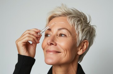 Sticker - A middle-aged woman with short blonde hair, smiling and applying face serum to her cheekbones. She has closed eyes against the light background of white walls