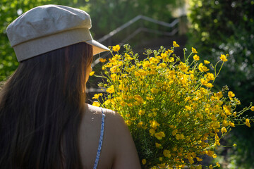 Girl or woman with long hair from behind in backlight with a bouquet of yellow buttercup flowers