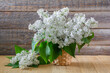 A bouquet of white lilac flowers in a wicker basket on a wooden background