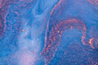 Blue and pink acrylic paints with shimmering golden glitter. Colorful liquid paint abstract background.