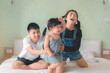 Elder asian sister and Elder brother play and dance with younger asian sister on a bed, Happy childhood.
