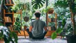 A man sits cross-legged on the floor in a yoga pose, surrounded by lush plants and sunlight.