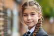 Portrait of a joyful young girl with braided hair, wearing a school uniform, standing outdoors with a blurred background, capturing the essence of childhood and education