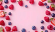 Frame made of fresh raspberries, blueberries and strawberries on pink background