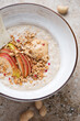 Bowl of oatmeal porridge with peanut butter and fresh apple, vertical shot on a beige granite background, middle close-up