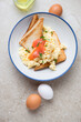 Toasts with scrambled eggs and smoked salmon served in a blue and white plate, vertical shot on a beige stone background, flat lay