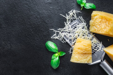 Poster - Parmesan cheese slices with basil leaves and grater on a dark stone background with copy space top view