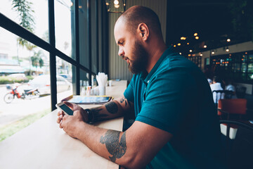 Fototapete - Young hipster guy checking new updates of social networks content via smartphone on break in cafeteria, creative male bolgger chatting with followers an share multimedia using mobile phone and wifi