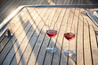 Two wineglasses on a yacht. Romantic picnic with wine at sunset. Travel in sea. Beautiful drinks, beverages on wooden deck in vacation. Enjoyment, relaxation on summer holidays. Still life