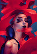A glamorous model with bold makeup poses amid vibrant red brush strokes.