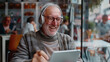 © DEDEED - Happy senior man using tablet and headphones to watch video online in a modern cafe.