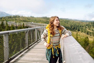 Young woman on wooden bridge with backpack among treetops. Concept of freedom, travel, lifestyle. 