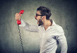 Side view of casual bearded man holding red telephone receiver and yelling in anger.