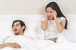 Snoring couple health asian man snore and sleeping at home while woman insomnia annoyed, bad noise cover ears with hand sleep problem apnea and relationship, wife looking at husband snoring in bed.