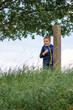 Little boy in nature, Child on a mountain covered with tall grass near a concrete pillar. The light blue sky in the background and the crown of lush branches of the oak tree above