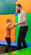 Happy bearded father with their little son jumping on a trampoline together at the entertainment centre.