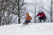A father plays with his son outside in the winter, he helps the child to go down the hill on a sled by pushing him