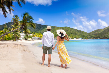 Sticker - Happy holiday couple with sunhats walks down a tropical beach surrounded by rain forest in the Caribbean, Antigua island