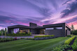 A charcoal-gray home at dusk, under a sky of purple and pink, stands surrounded by a pristine lawn and beautifully arranged plants.
